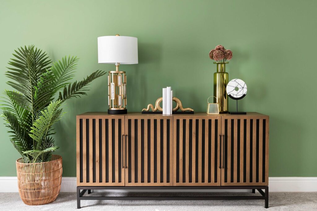 green wall and wooden sideboard with gold accessories and lamp
